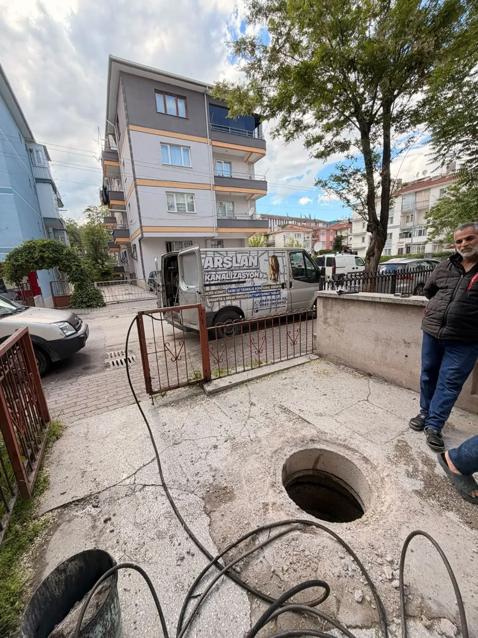 Apartman bahçesinde kapağı açılmış rögar ve serilmiş hortum hattı, arkada Arslan servis aracı