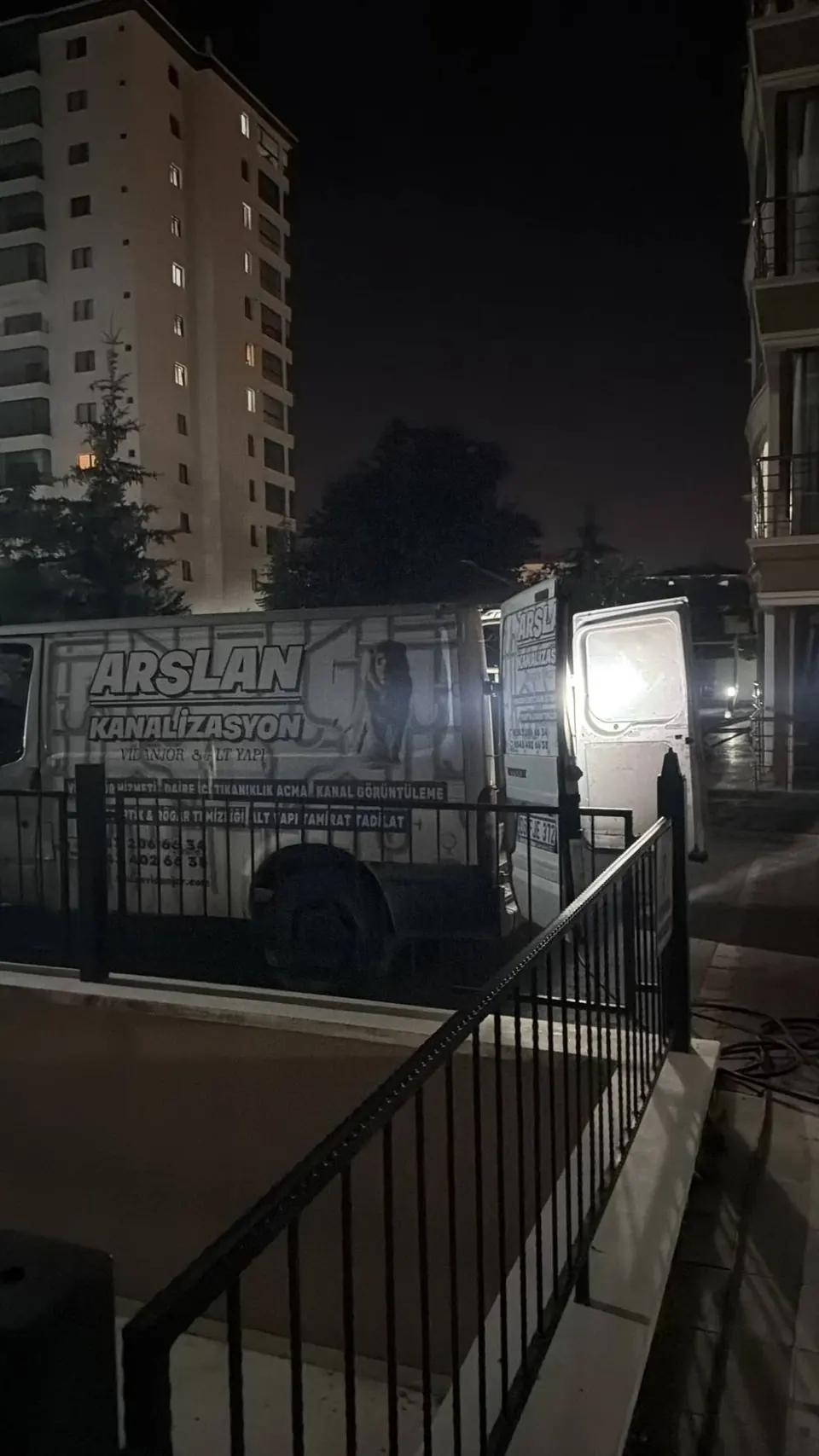 Gece bir site önünde arka kapısı açık, ışıkları yanan servis aracı