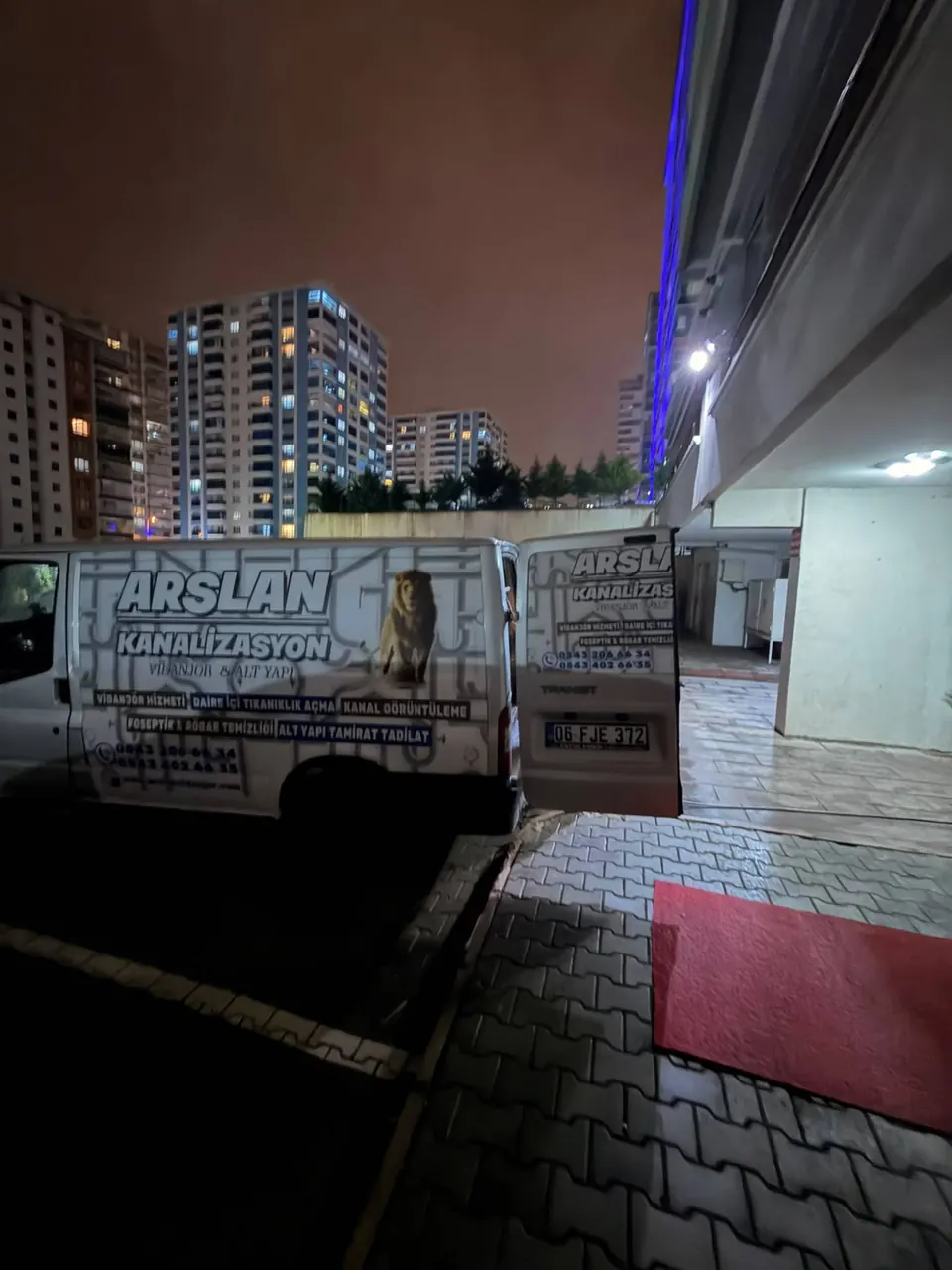 Gece yüksek blokların arasında site girişinde açık kapılı servis aracı