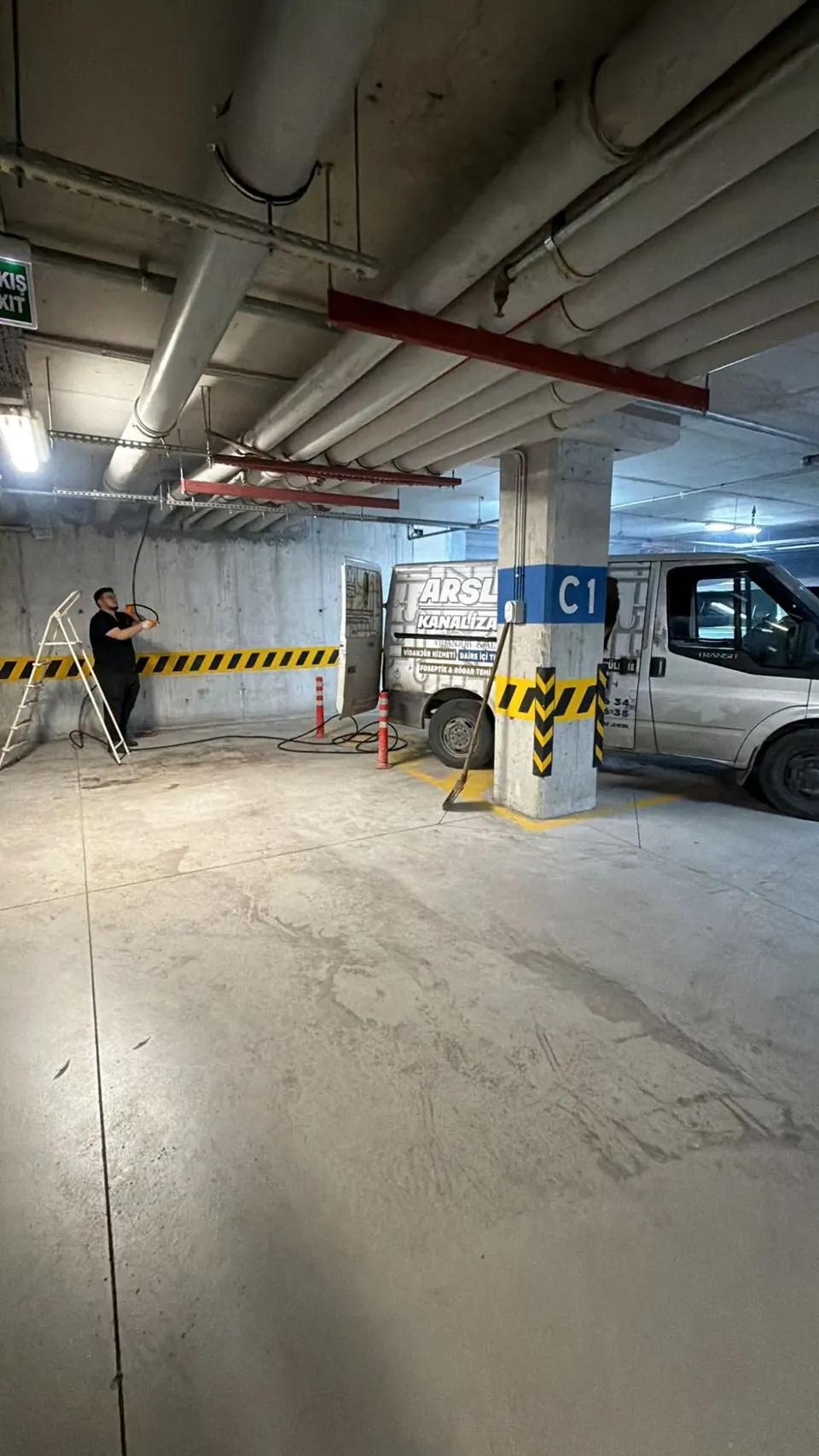 Kapalı otoparkta tavan boyunca geçen hatta merdivenle müdahale eden teknisyen