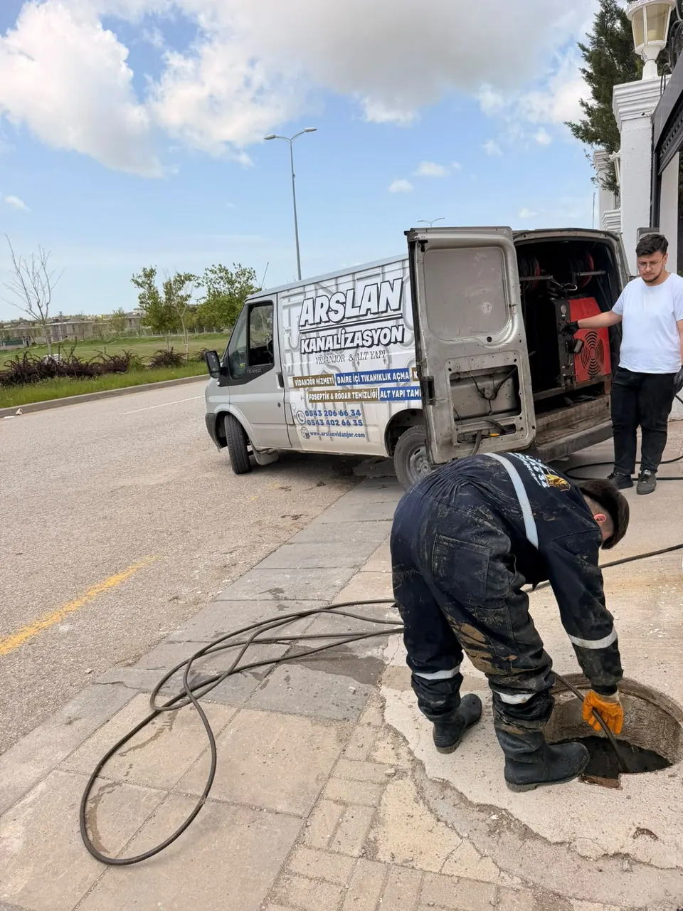 Yol kenarındaki rögarda hortumla çalışan teknisyen, araçta makara ve pompa
